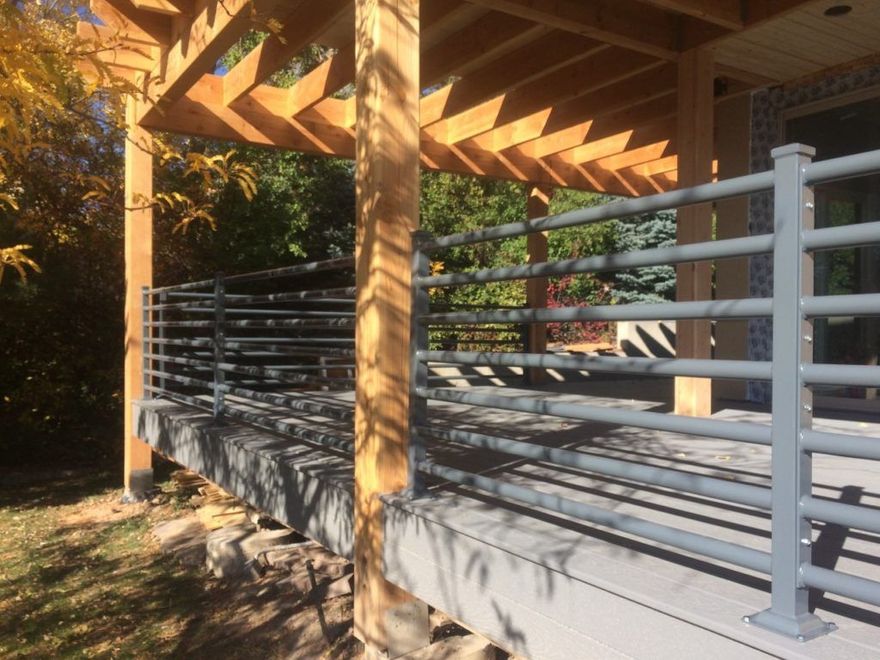 Gray deck railing under a wooden pergola on a sunny day.