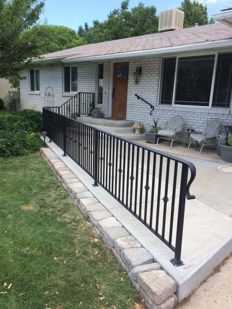 Black iron ramp with railing leads to the front door of a white brick house.
