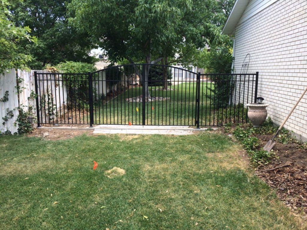 Black metal fence with gate in grassy backyard, against a white brick house.