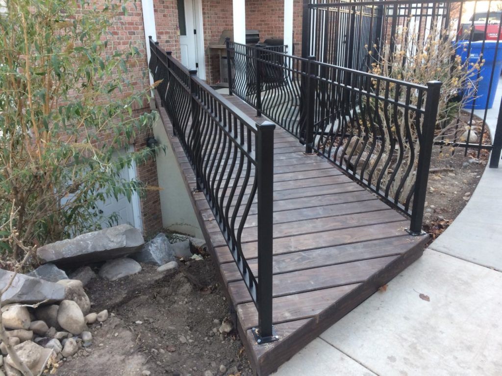 Black metal ramp with wavy railings and dark wood flooring leading to a doorway.