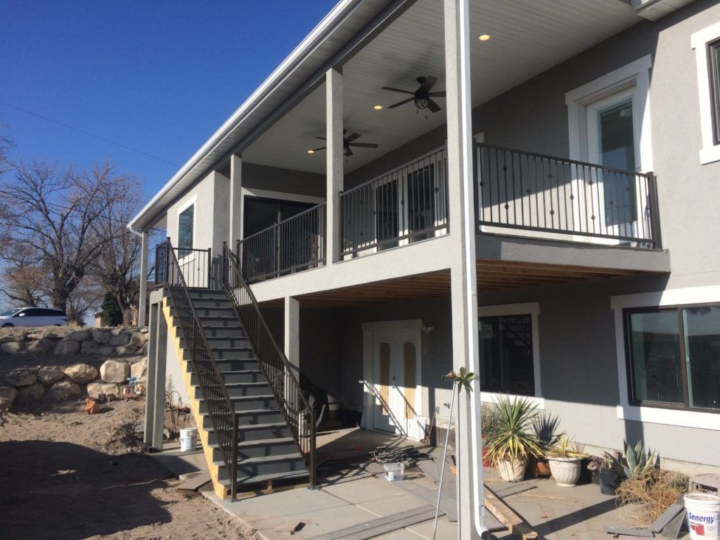 Two-story house with a covered porch. Black railings, gray exterior, and a staircase leading to the upper level.