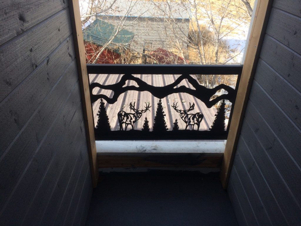 Black metal railing with elk silhouette over an outdoor view, framed by dark wood.