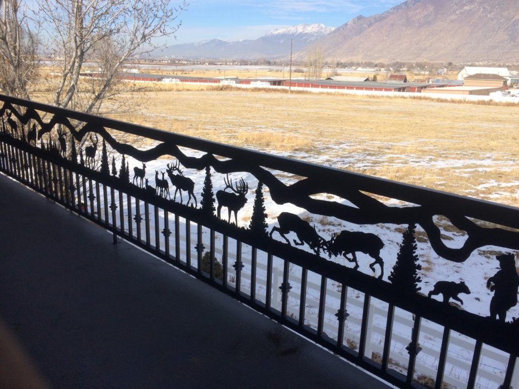 Black metal balcony railing with wildlife silhouettes overlooking a snowy field and mountains.