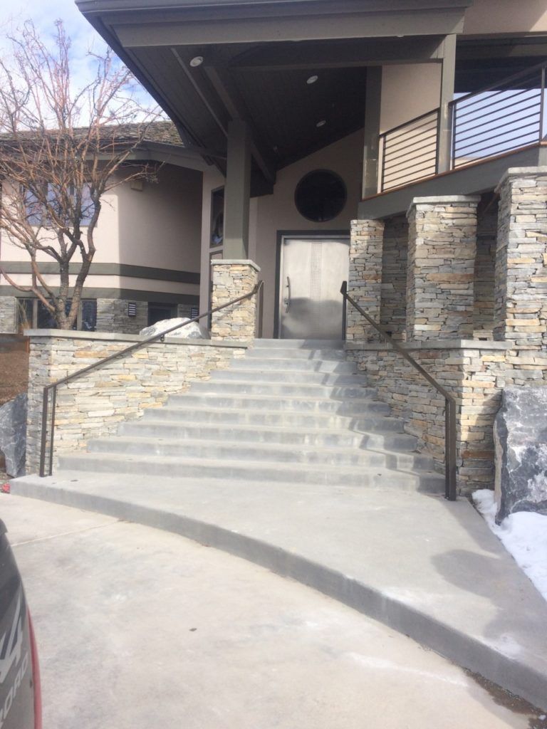 Exterior view of a building with stone facade, concrete stairs, and metal railings leading to the entrance.