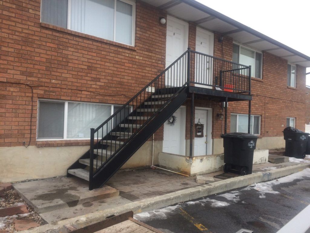Exterior of a brick apartment building with black metal stairs leading to upper-level doors.