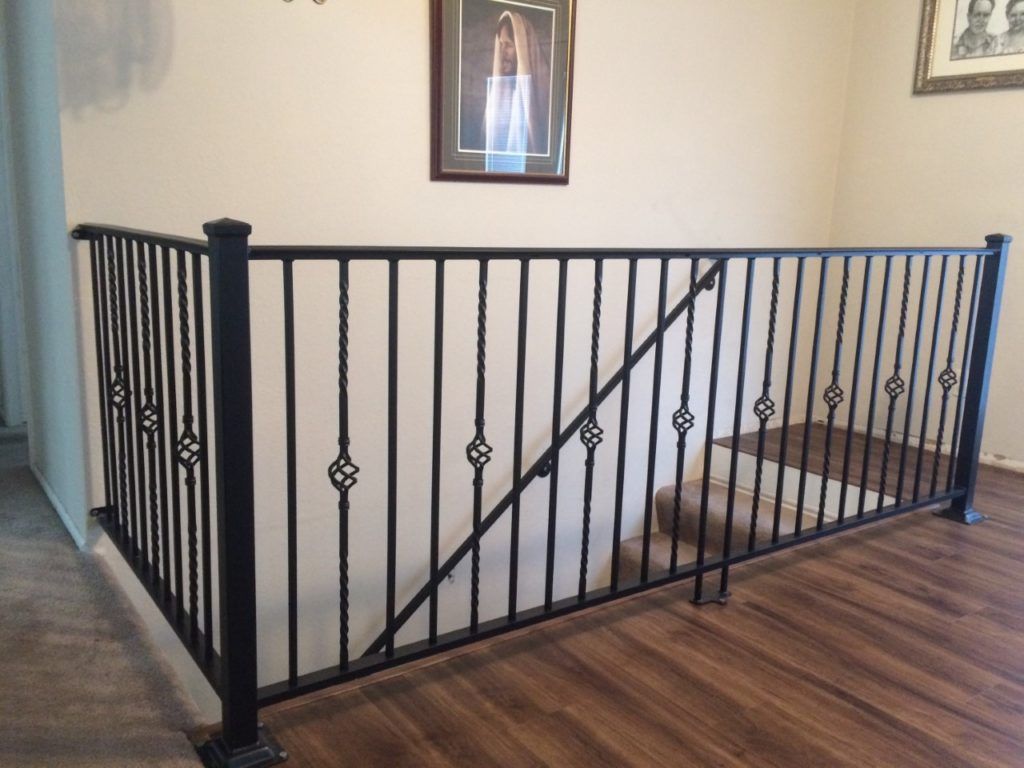 Black metal railing on a landing with dark wood flooring, against a light-colored wall with framed art.