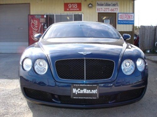 A bentley is parked in front of a coca cola machine