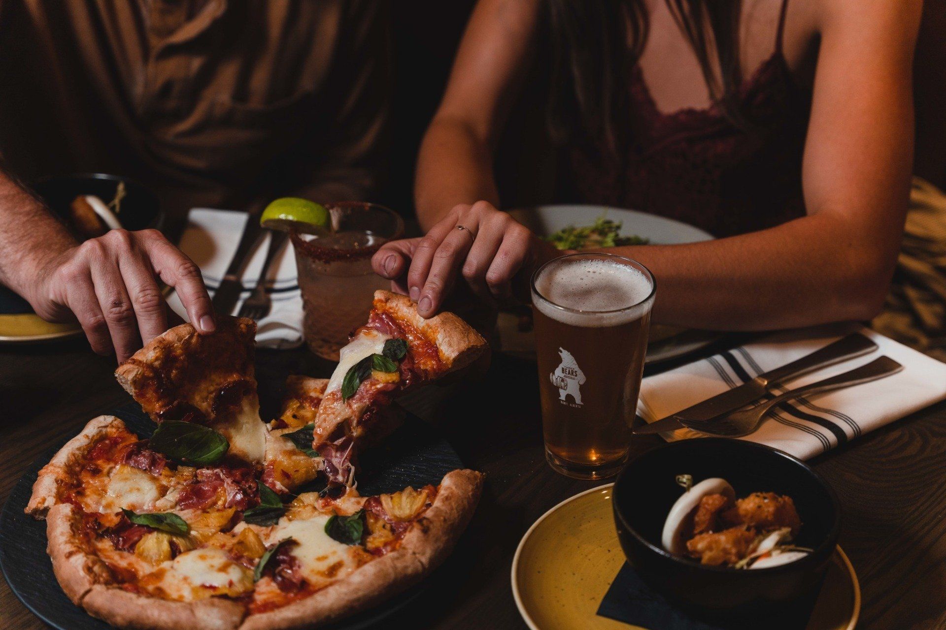 Two people eating pizza and drinking beer.