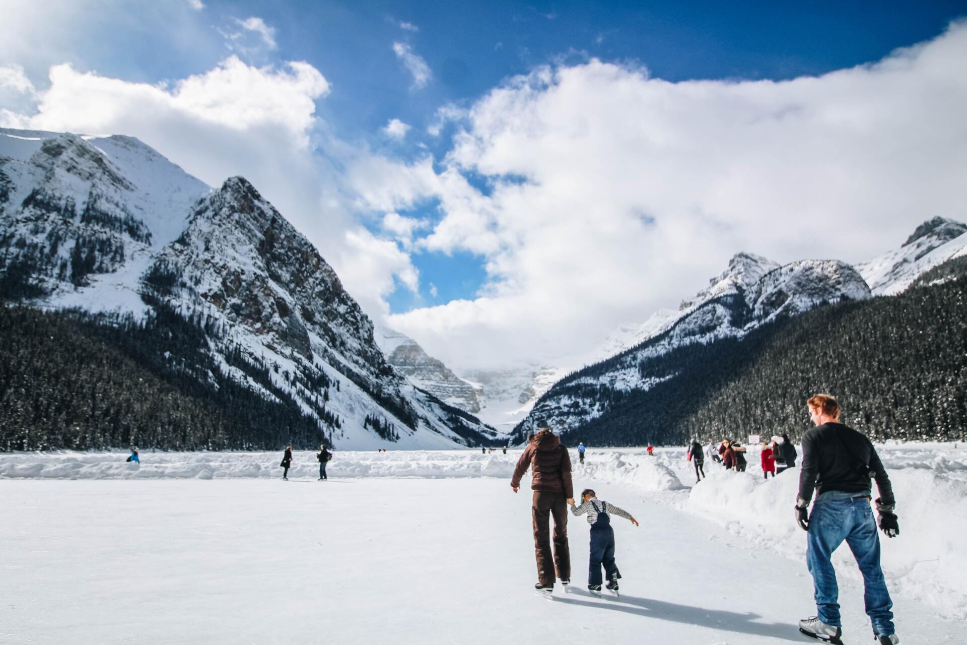 Skaters on a frozen lake in Banff National Park surrounded my mountains.