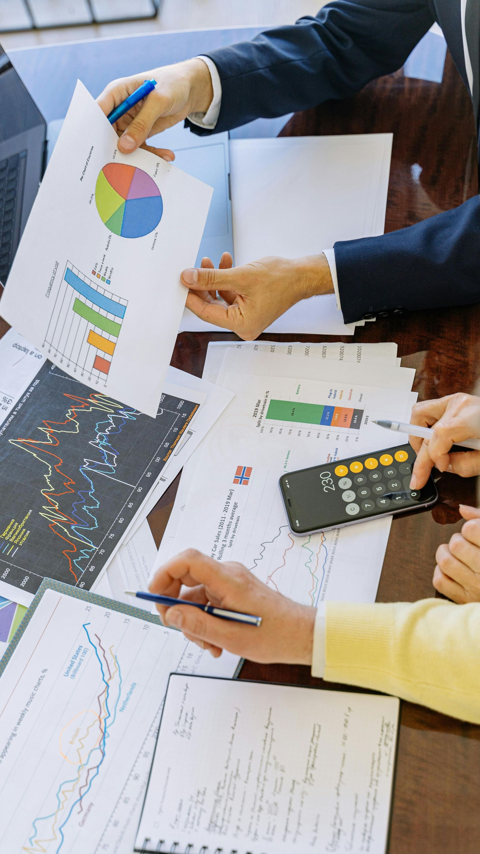 People reviewing reports, including graphs and a calculator, on a table.