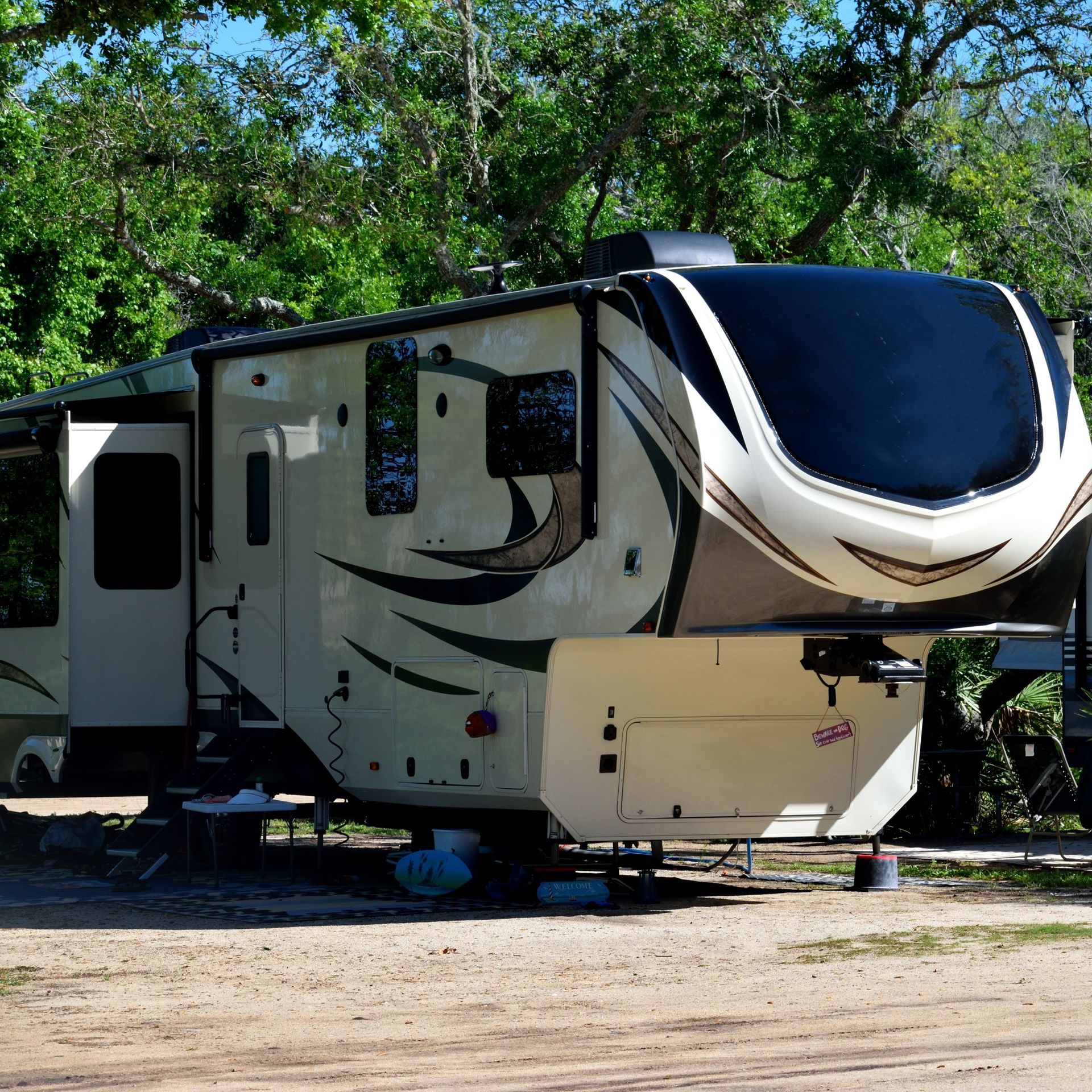 Beige and black RV parked in a campground. Trees are in the background.