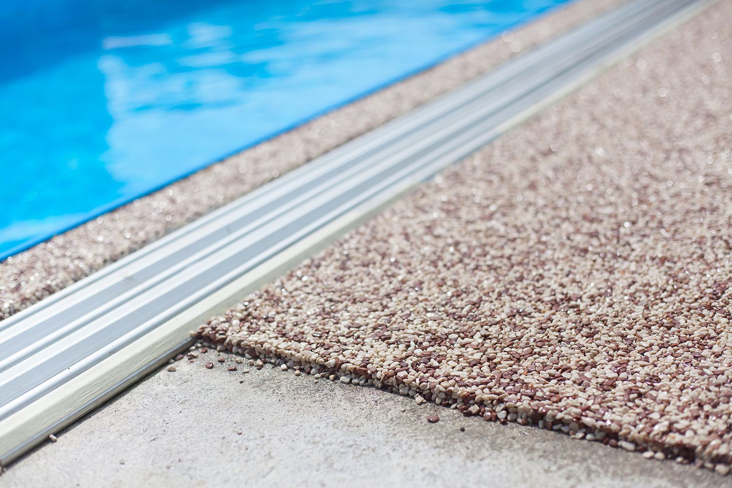 A close-up of beige and brown coloured aggregate concrete around a pool’s edge.