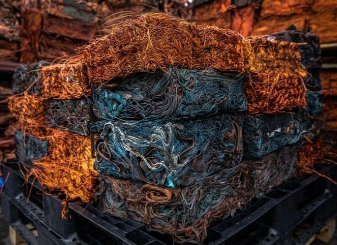 Compressed copper wire ready fro recycling, orange and blue, stacked on a pallet.