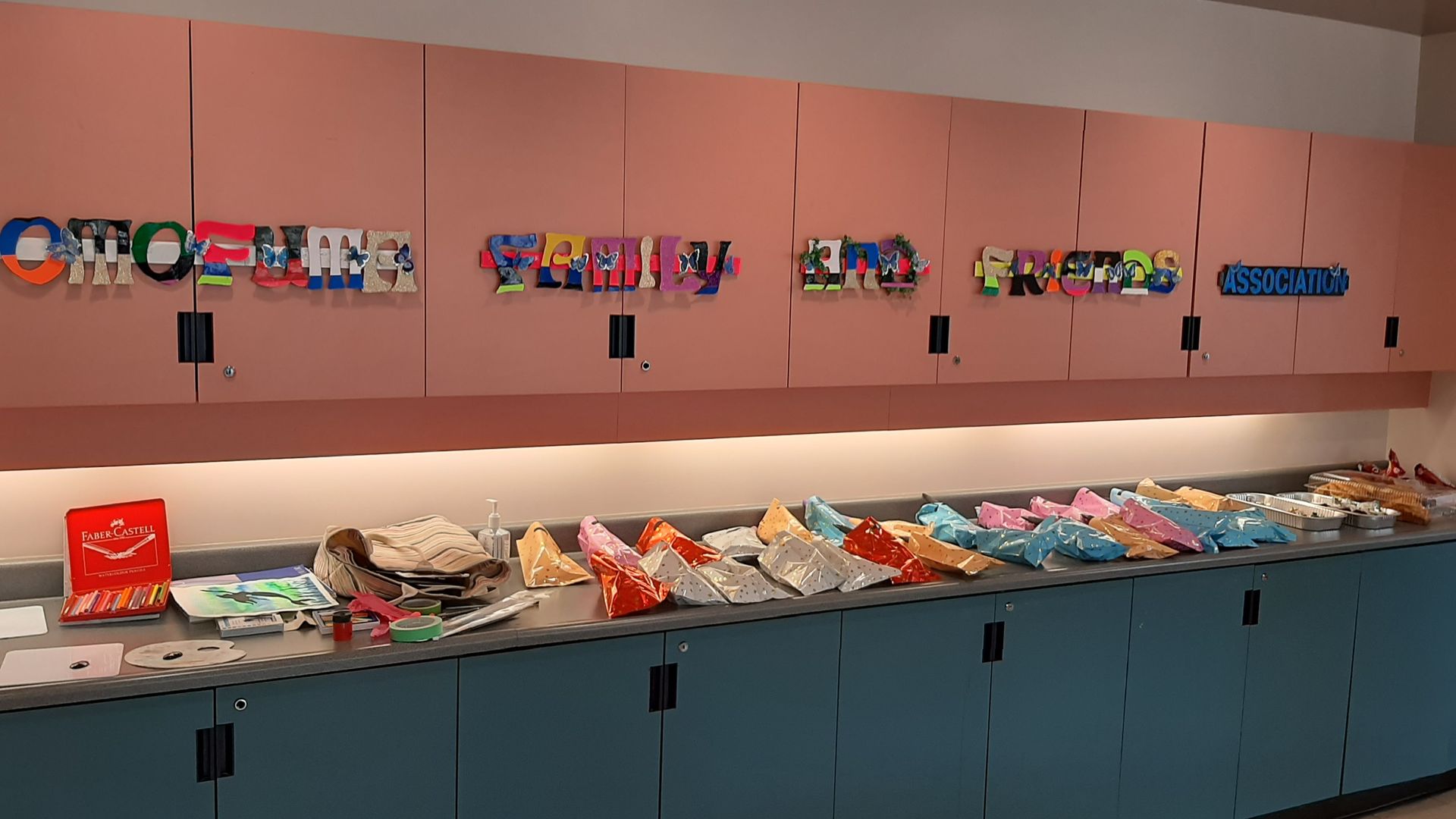 Pink cabinets with colorful art; blue cabinets below with bags and supplies.