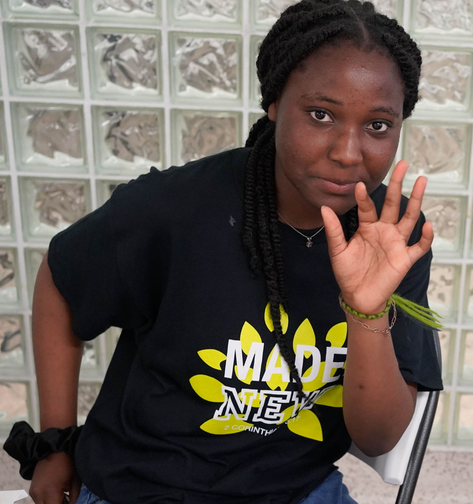 Young Black woman with dark braids, black tee with yellow graphic, holding up her hand.
