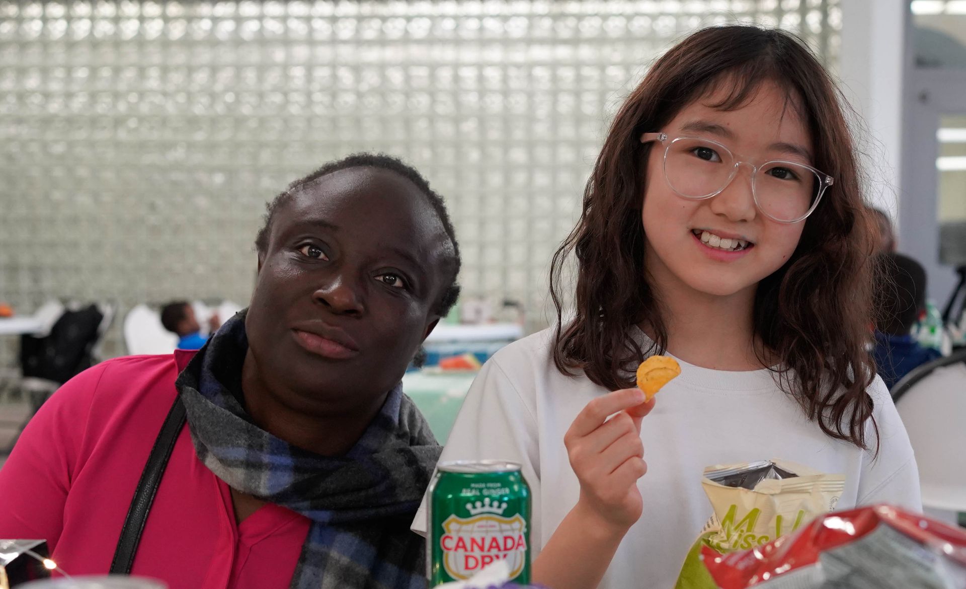 Two women smiling at camera, one holding a snack. One has dark skin, the other is East Asian.