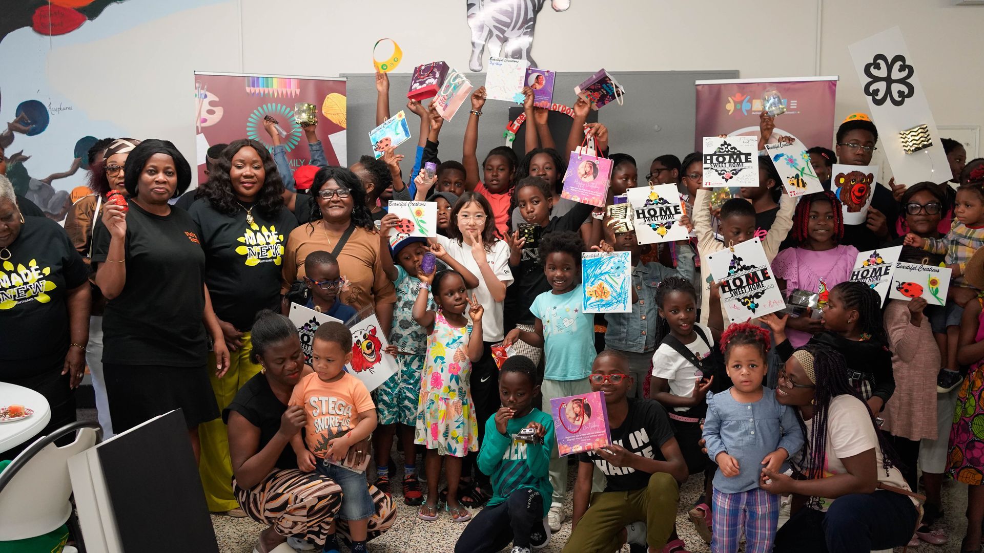 Large group of children and adults, mostly Black, holding up artwork in an art studio.