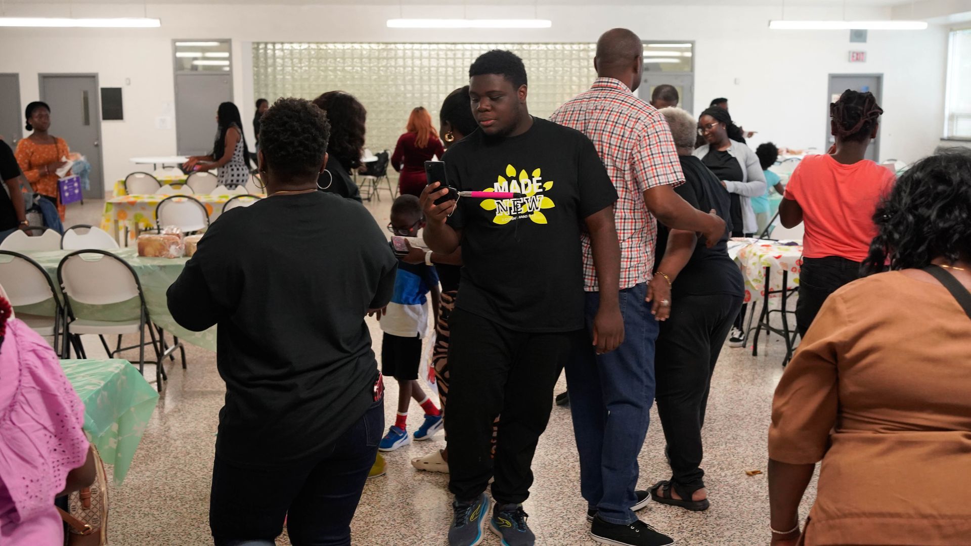 People at an indoor gathering. Several adults and children socialize, some looking at phones.