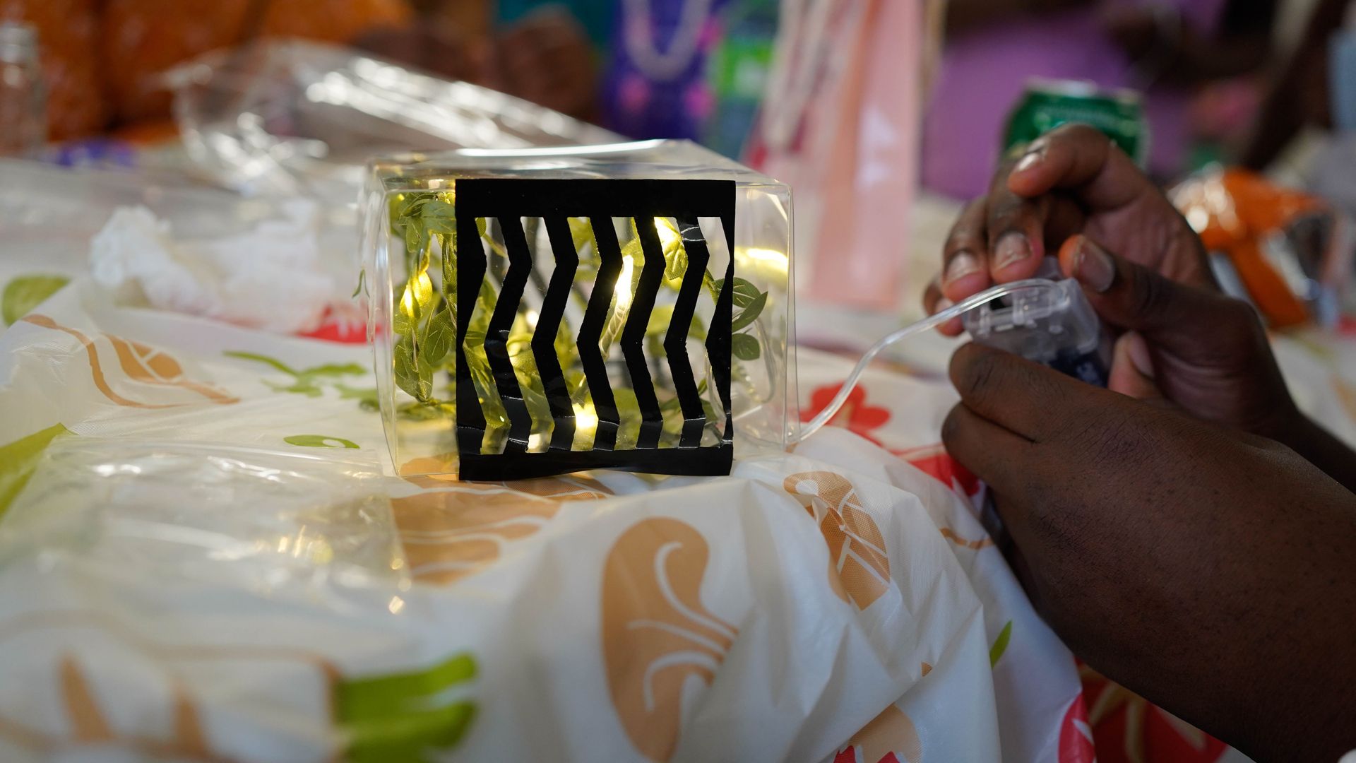 Person assembling a glowing, patterned cube on a patterned tablecloth.