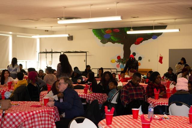 People at tables covered in red and white checkered tablecloths, in a room with a painted tree mural.