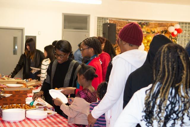 People at a food buffet. Women and children serve food, smiling, at a community event.