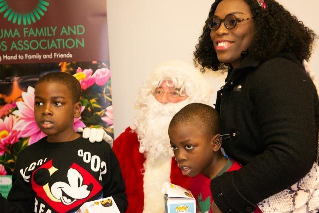 Two young boys, a woman, and Santa Claus posing. Santa has white beard, boys are looking at something, and the woman is smiling.
