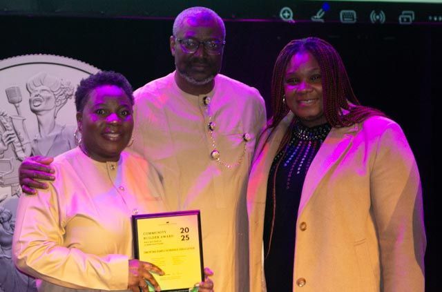 Three people at an event; a woman holding an award, flanked by a man and woman.