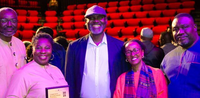 Group of five people smiling for a photo in a theater. Red seats in the background.