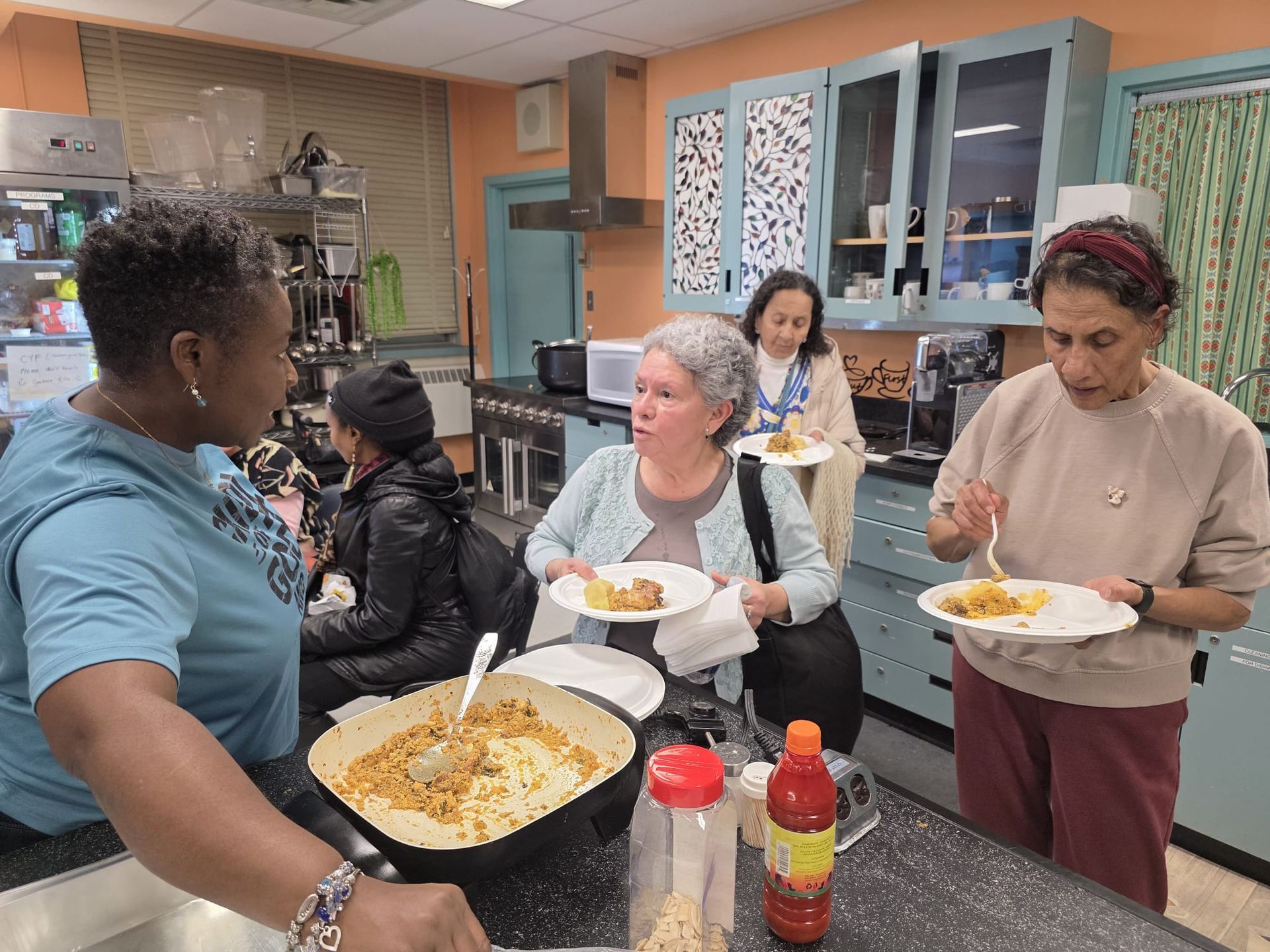 People in a kitchen eating food from plates. One person serves from a large pot.