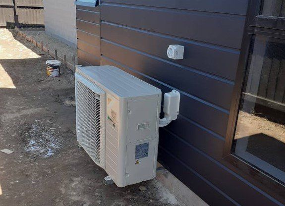 Outdoor heat  pump unit installed on black external wall.