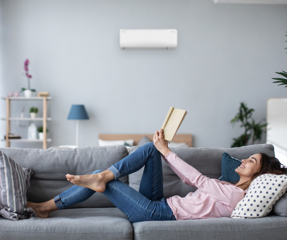 Woman reading a book on the sofa, heat pump in the background.