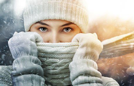 Woman in snow with scarf up to her mouth wearing hat and gloves