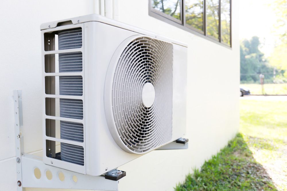 A White Air Conditioner is Mounted on the Side of a Building — Bradmark Appliance Service in Garbutt, QLD
