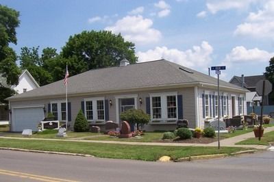 A one-story building with a gray roof and blue shutters on a corner lot, with an American flag.