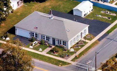Aerial view of a light beige building with a dark roof and a small parking area in front.