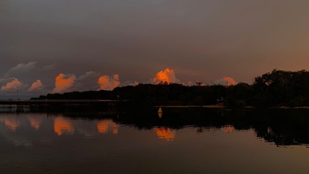 A Sunset Over A Lake With Trees In The Foreground And A Bridge In The Background — Kingscliff Pool Shop In Pottsville, NSW