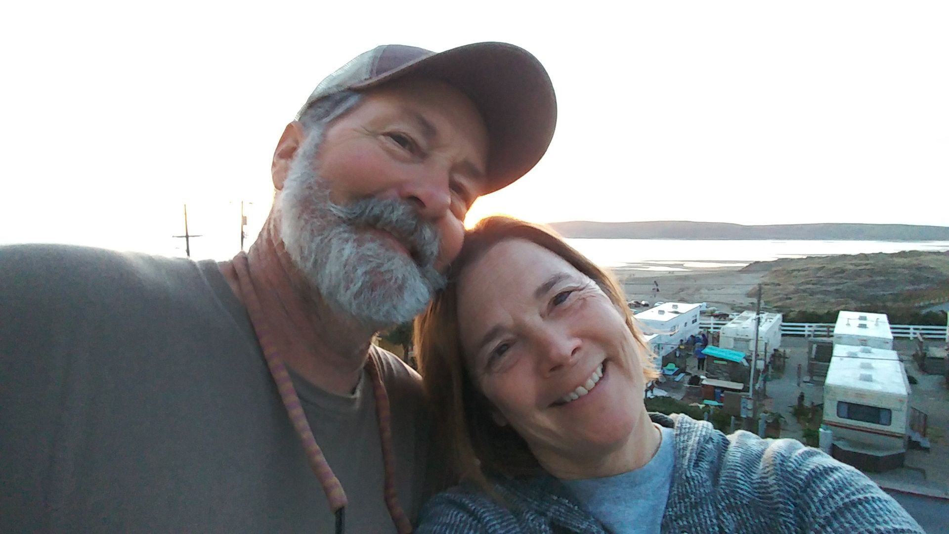 A man and a woman are posing for a picture in front of a body of water.