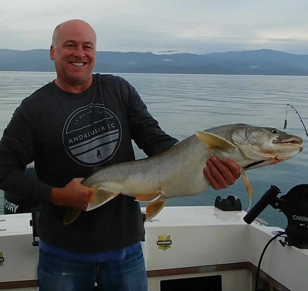 A man on a boat holding a large fish and wearing a shirt that says andrews fc