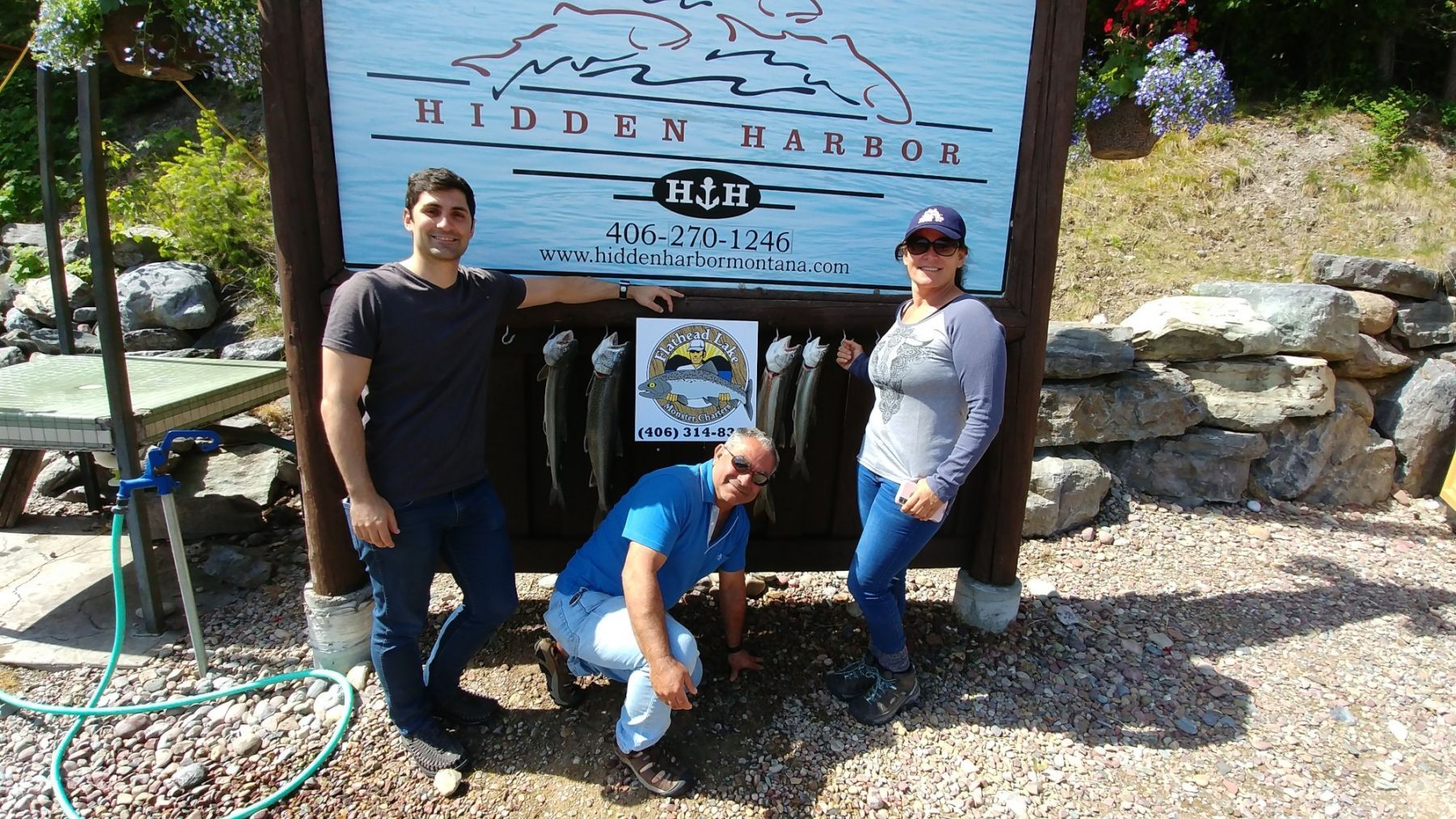 Three people pose in front of a sign that says hudson harbor