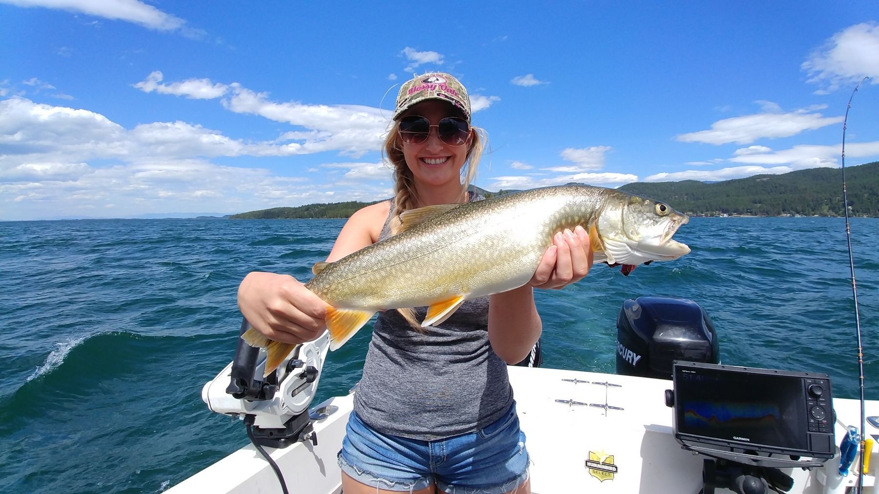 A woman is holding a fish on a boat in the water.
