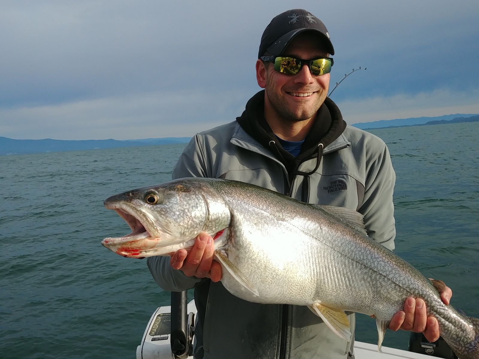 A man wearing sunglasses is holding a large fish in his hands