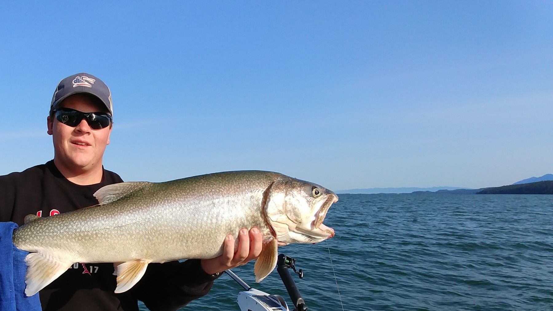 A man is holding a large fish in front of a body of water.