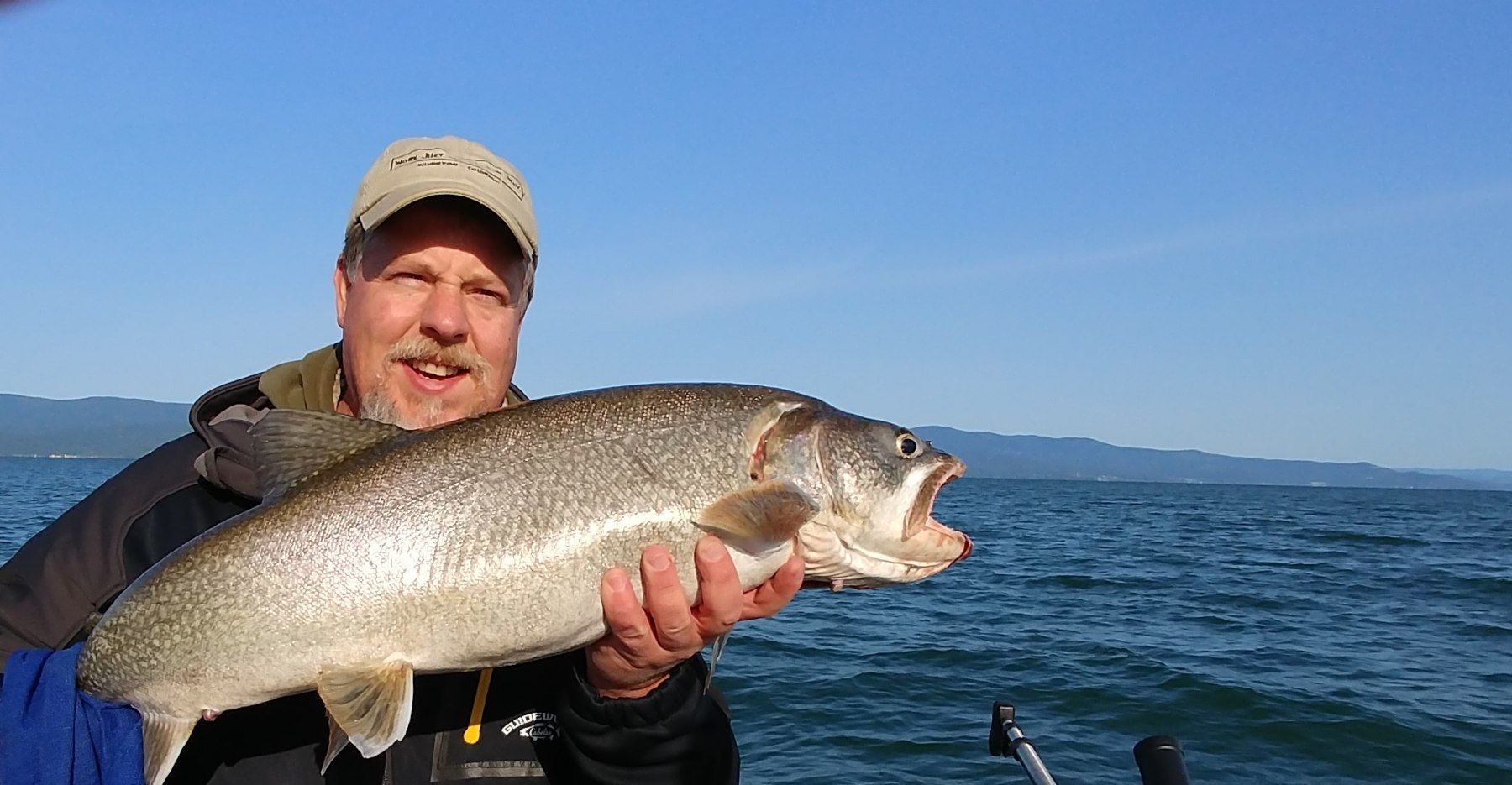 A man is holding a large fish in front of a body of water.