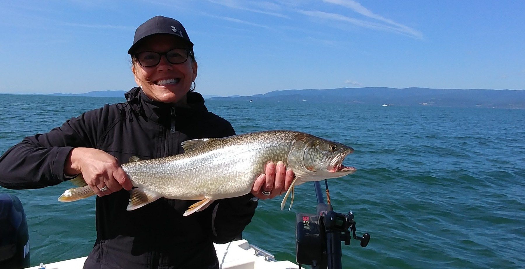 A woman is holding a large fish on a boat in the water.