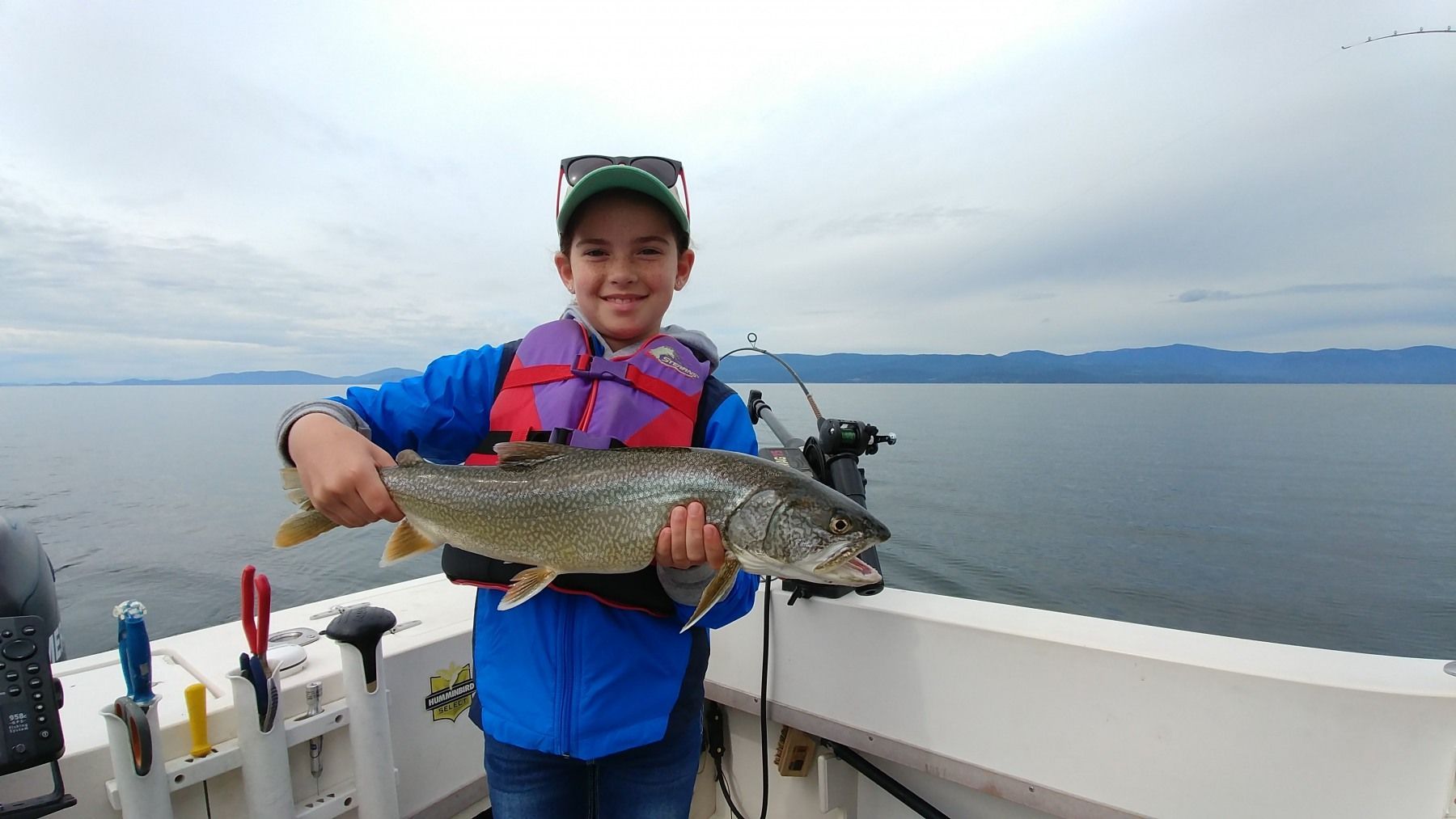 a little girl is holding a large fish on a boat overlooking a lake