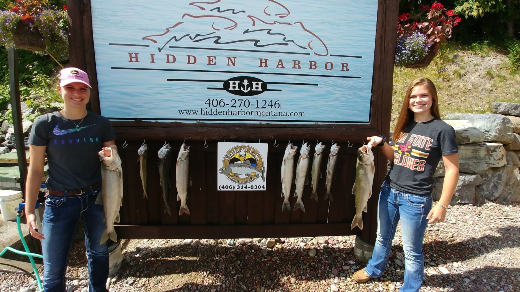 Two women holding fish in front of a sign that says hidden harbor