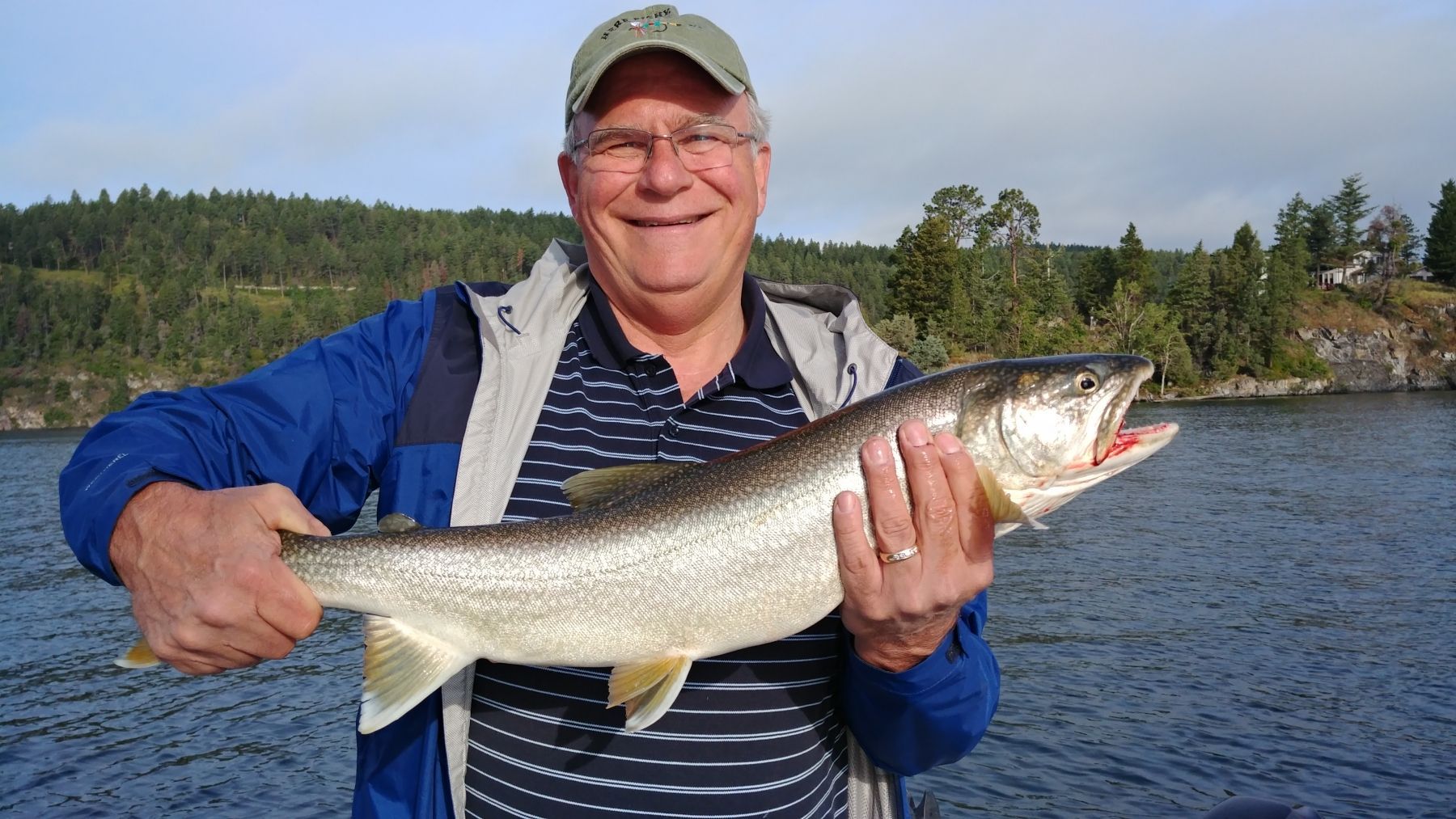 A man is holding a large fish in his hands in front of a body of water.