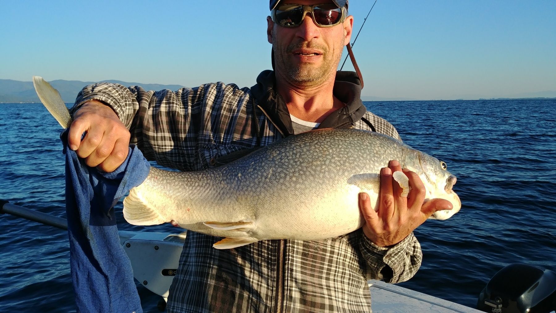 A man is holding a large fish on a boat in the ocean.
