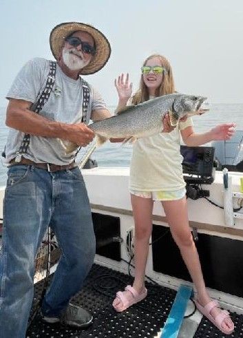 A man and a girl are standing on a boat holding a large fish.