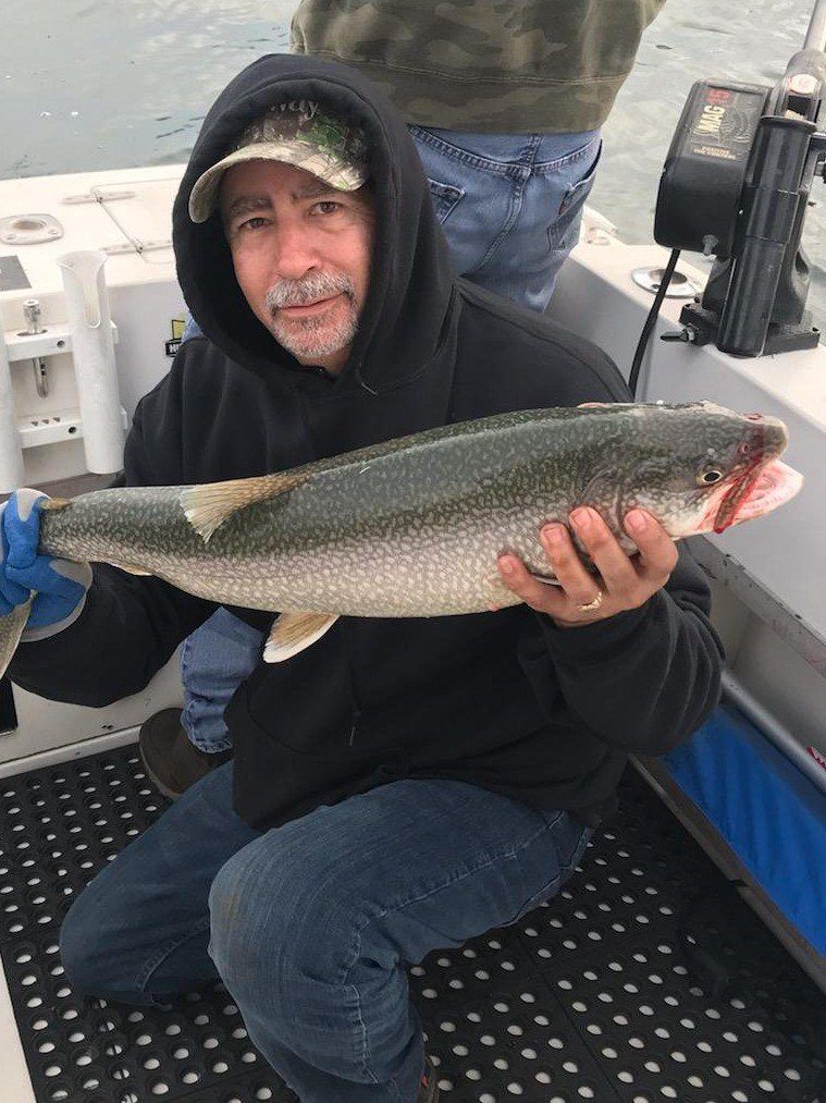 A man is kneeling on a boat holding a large fish.